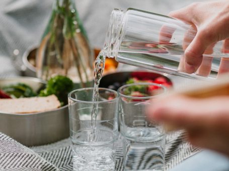 Picknickdecke auf der Wassergläser stehen, in welche gerade Wasser gefüllt wird.